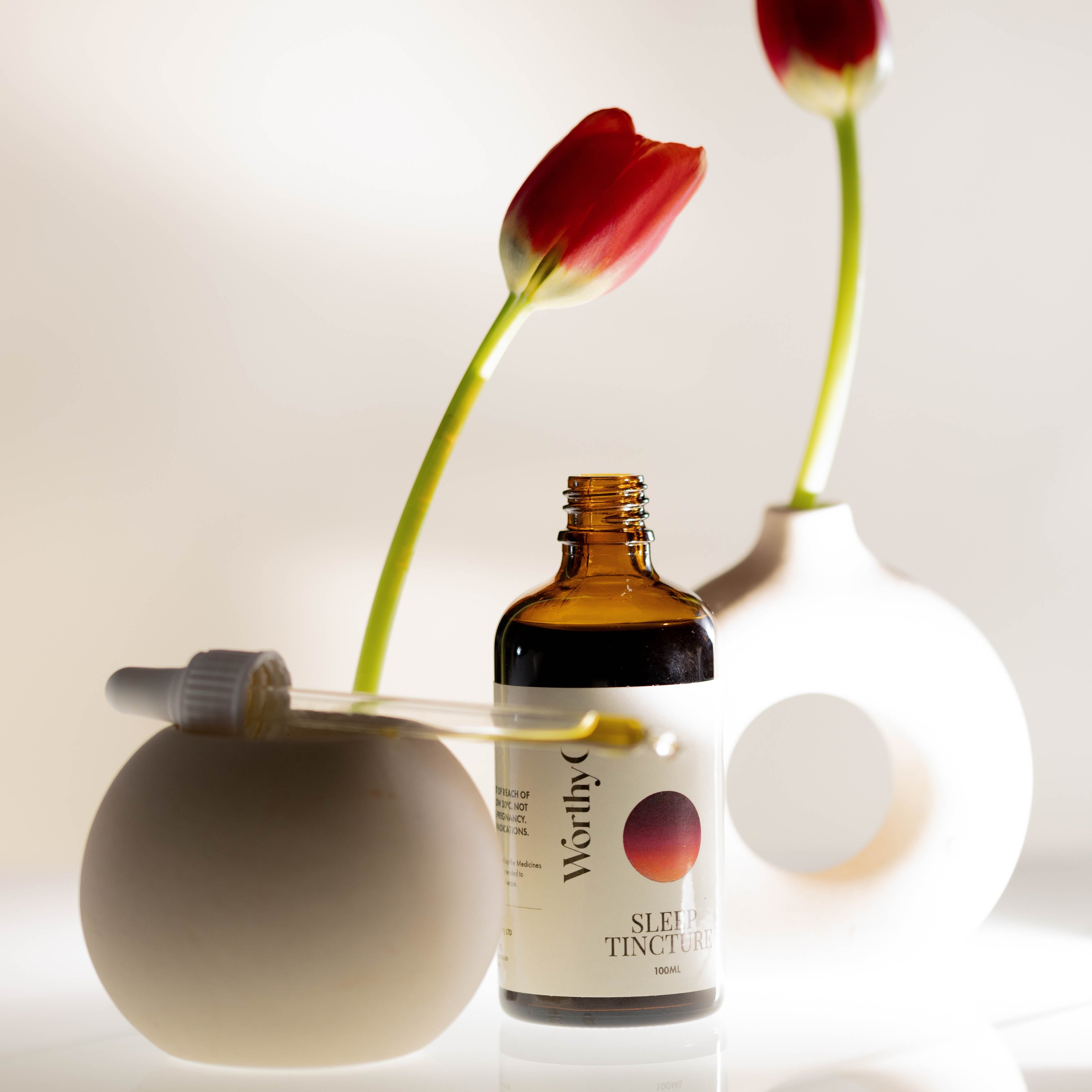 Bottle of Worthy Skin Tonic with two red tulips in white vases on a light background